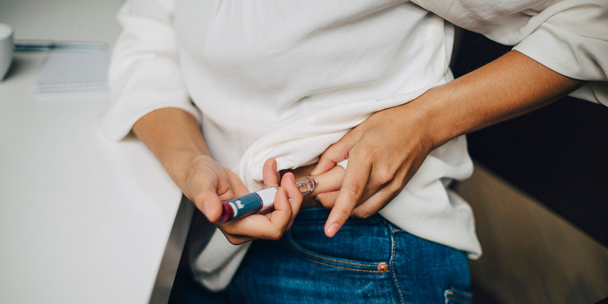 Kvinna sitter och har dragit upp sin tröja lite för att injicera läkemedel i magen. 