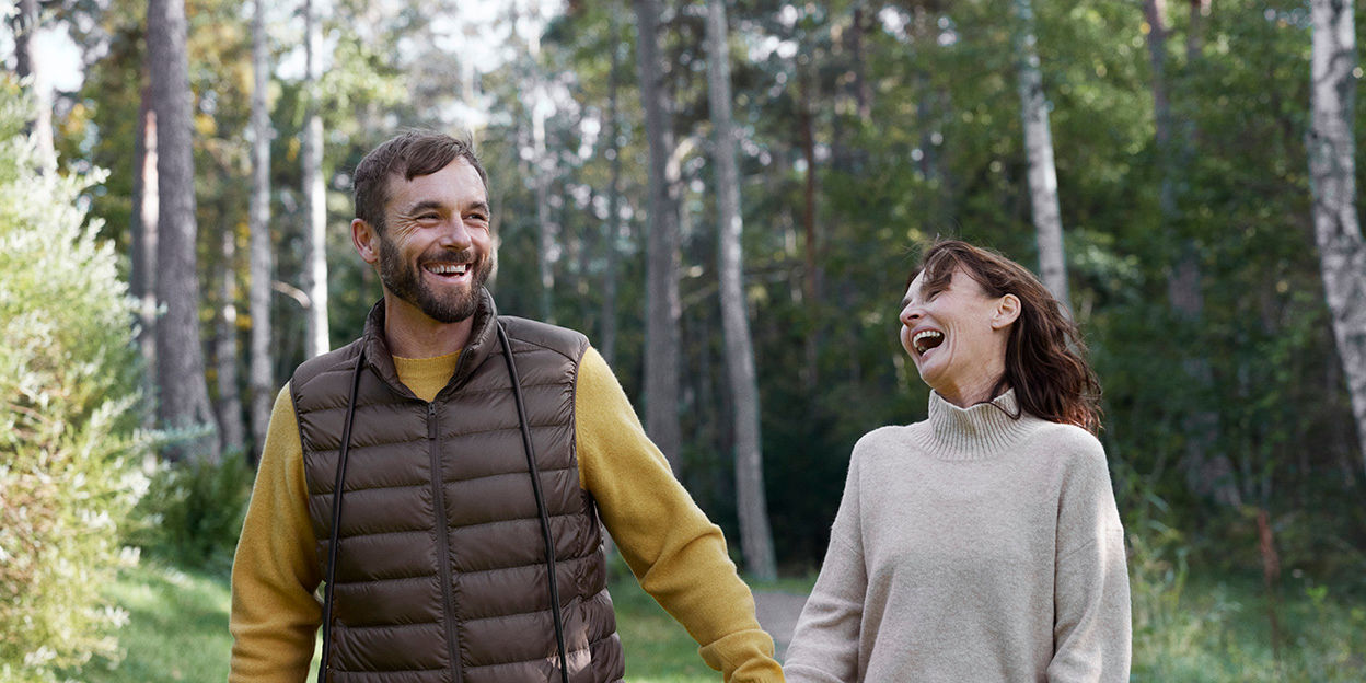 Man och kvinna på promenad på en skogsväg. De är galada och skrattar och omges av många björkar. 