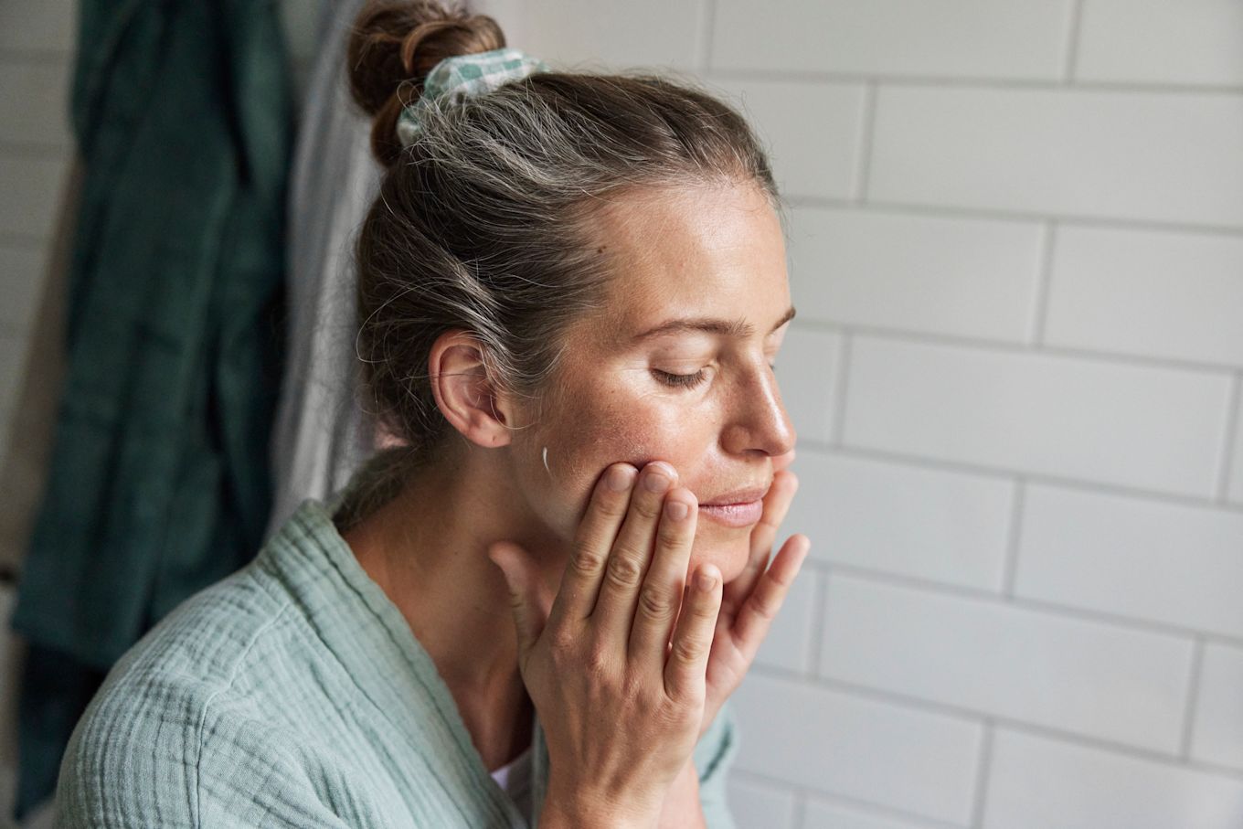 Kvinna står med uppsatt hår och smörjer in ansiktet i badrummet.