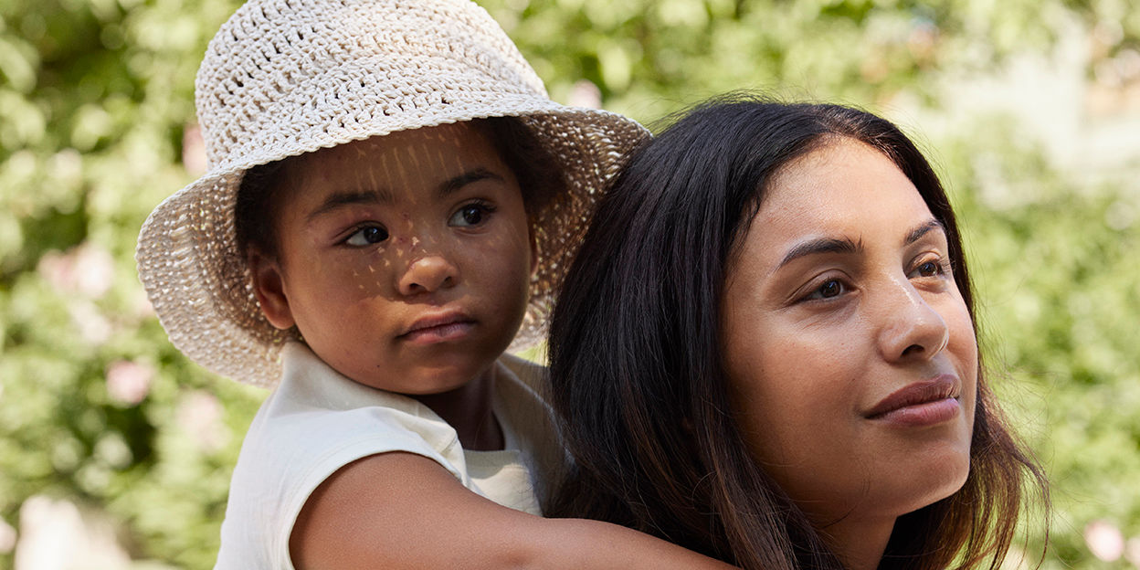 Barn i solhatt rider på sin mammas rygg en solig dag.