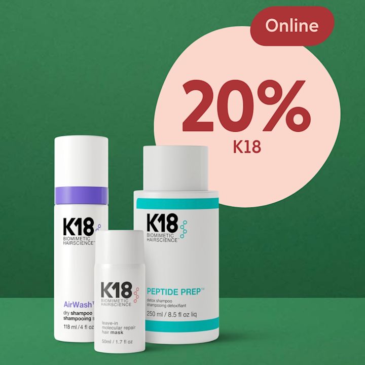 Tre K18 hårvårdsprodukter står på en grön yta med en grön bakgrund och en rosa cirkel med texten "20% K18 Online".