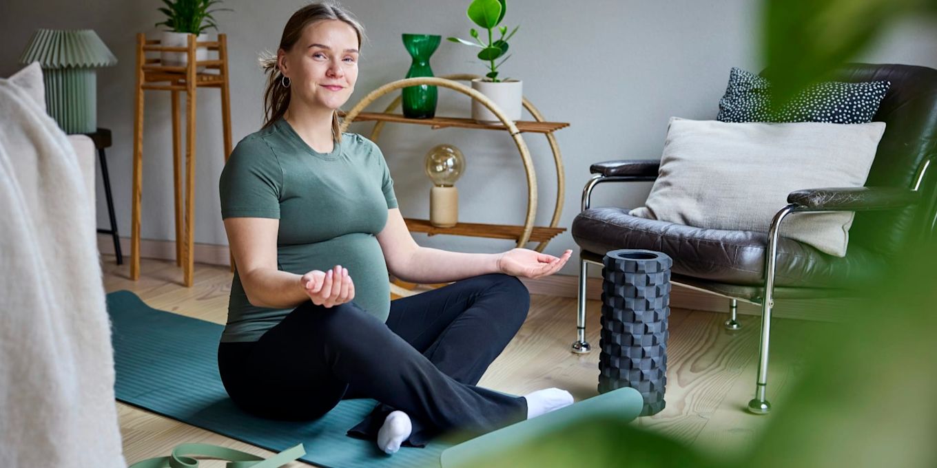 Gravid person tränar hemma på träningsmatta. Bilden illustrerar trygg träning och fysioterapi under hela graviditeten.