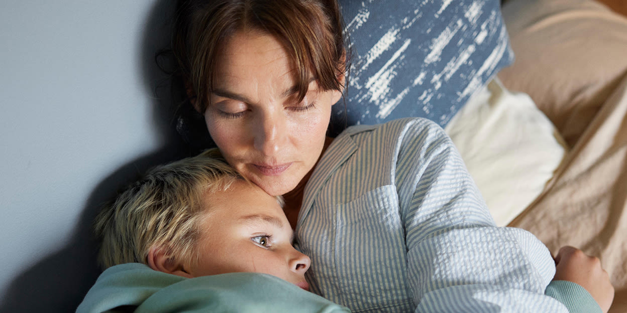 Mamma och son ligger i sängen och vilar och kramas. 