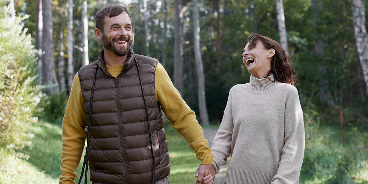 Man och kvinna ute i skogen skrattar och håller varandra i handen.