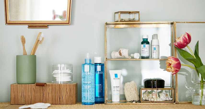 På en byrå står en blanding av olika produkter från La Roche-Posay, tillsammans med tandborstar, bomullsrondeller och röda tulpaner. På väggen ovanför hänger en spegel.