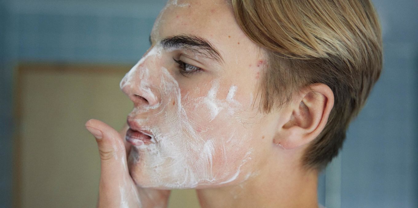 Närbild på en tonåring som applicerar ansiktskräm på kinden i ett badrum. 