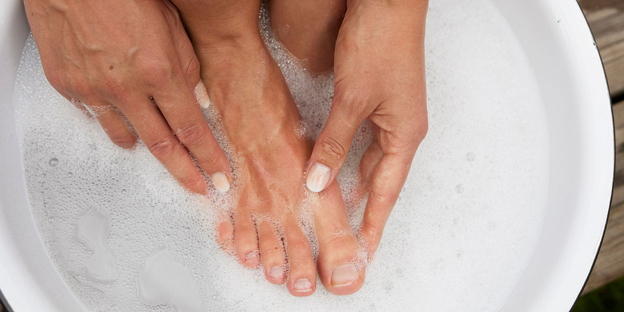 Två fötter syns en en badbalja med bubblor, bilden ger uttryck för self care