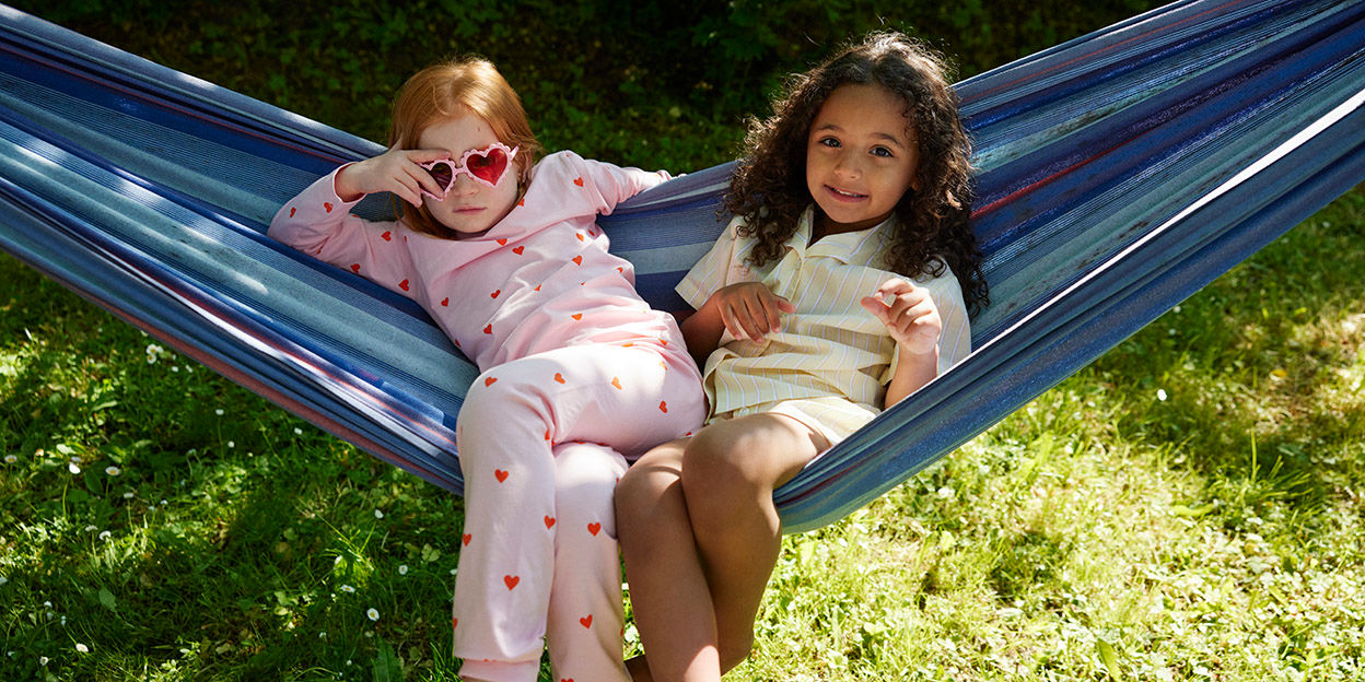 Två flickor sitter i hängmatta i trädgården.
