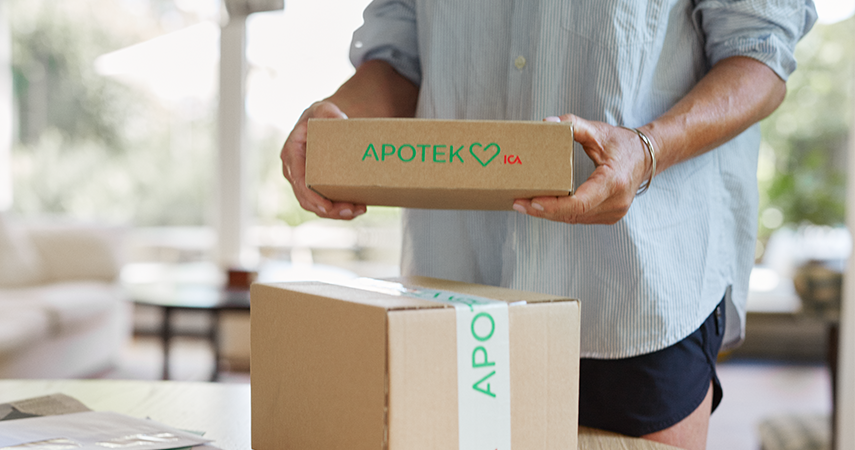 En person står och håller i ett paket från Apotek Hjärtat. Ett annat paket ligger bredvid på bordet.