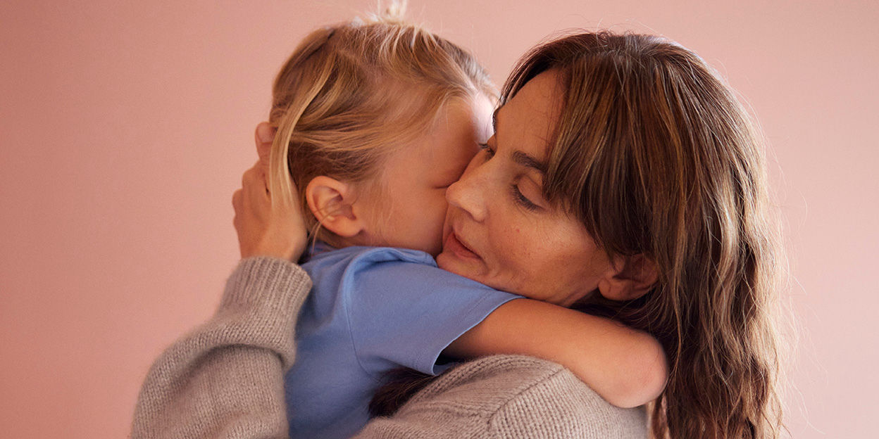 Mamma håller sitt barn i famnen, de kramar om varandra. 