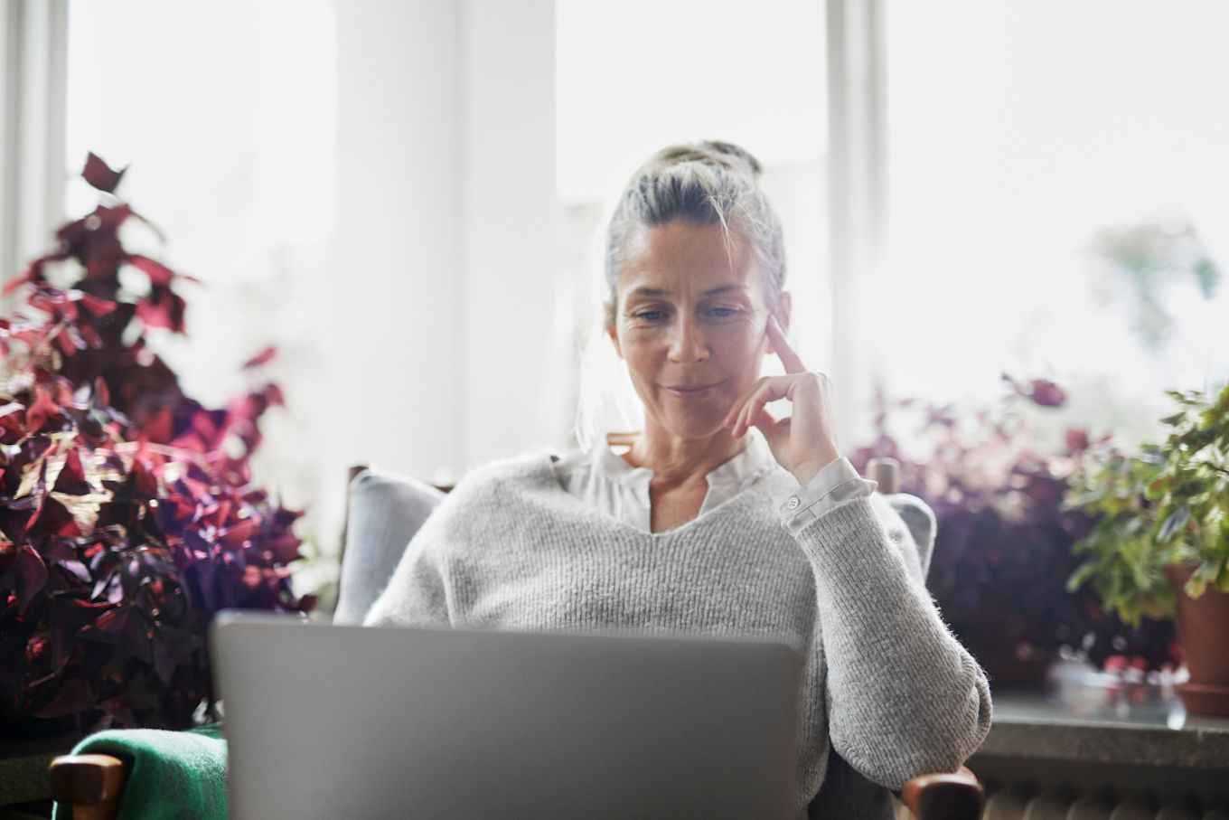 Kvinna sitter i fåtölj och tittar på en bärbar dator i sitt knä.
