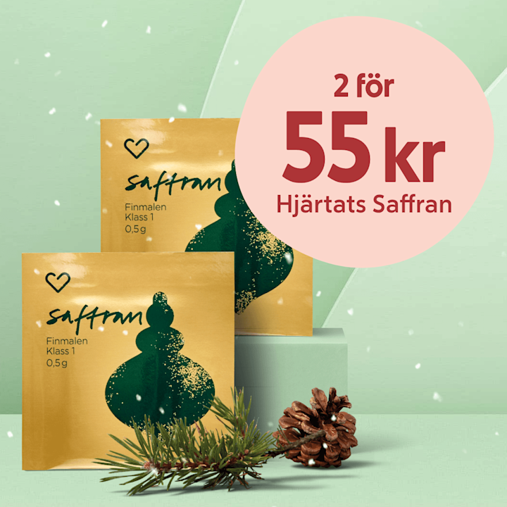 Två guldgula påsar saffran med grön julgransillustration placerade på mintgrön podie med en tallkvist och kottar framför, cirkelformad rosa prislapp "2 för 55 kr Hjärtats Saffran" uppe till höger.