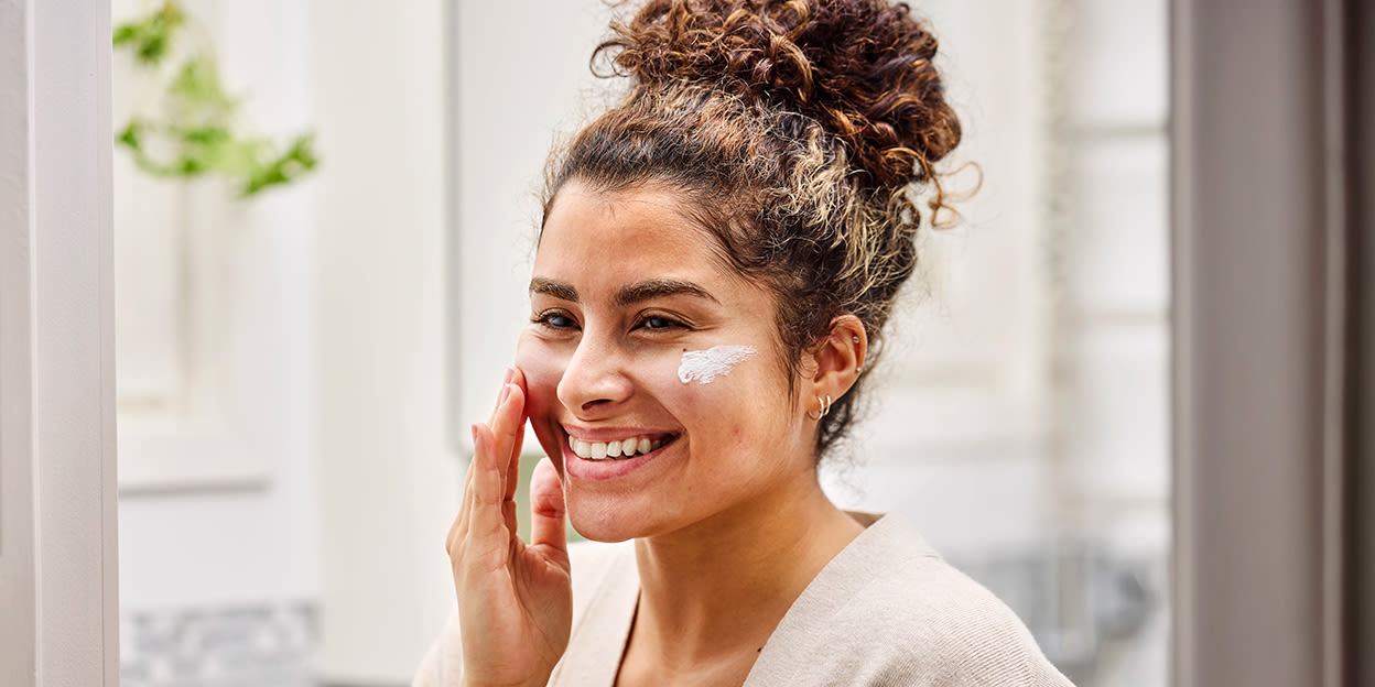 Kvinna står och smörjer in ansiktet med solskydd.