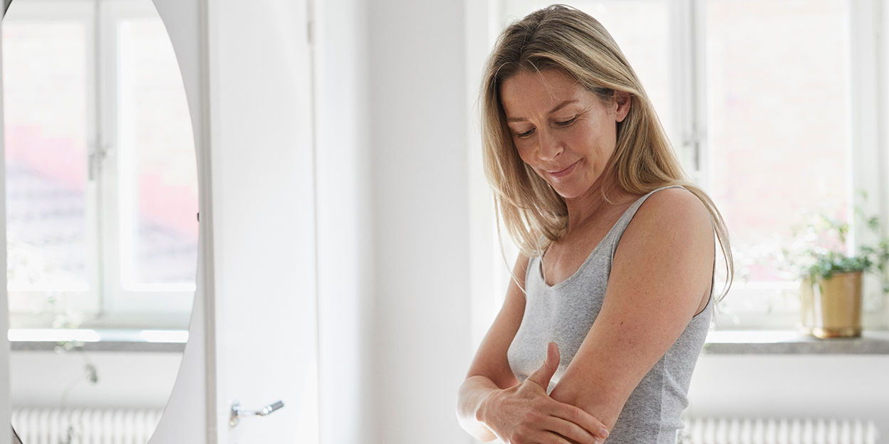 Kvinna står i badrum och kollar snett nedåt. 