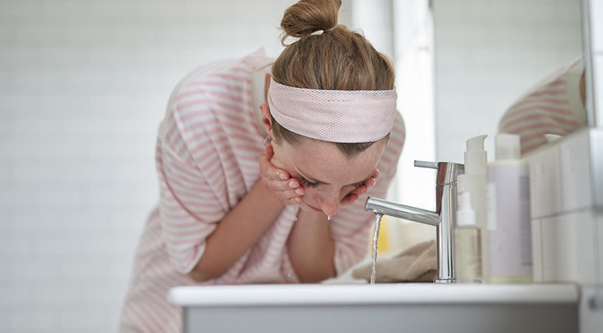 Tjej lutar sig över handfatet i badrummet och tvättar ansiktet.