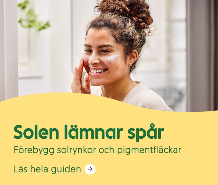 Kvinna ler och applicerar solkräm på kinden framför en spegel i ett ljust rum. Text: Solen lämnar spår. Förebygg solrynkor och pigmentfläckar.