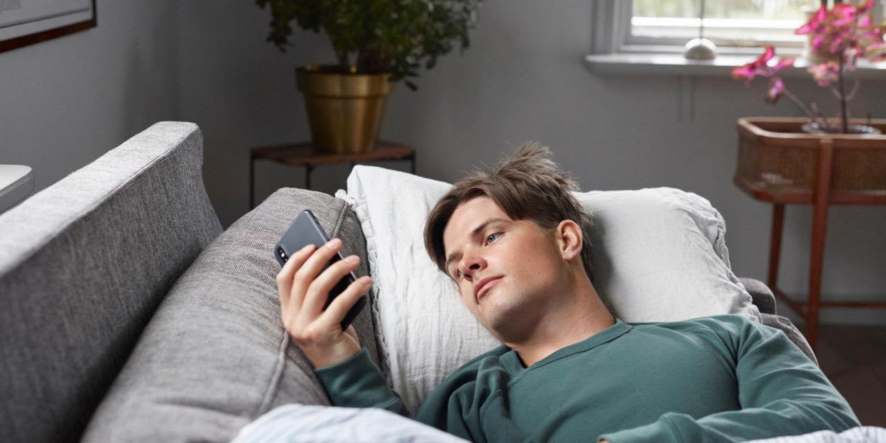 Man ligger på soffan och kollar på sin telefon.