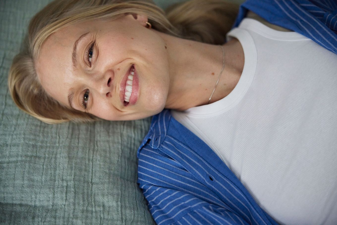 Kvinna ligger på en säng och ler stort.