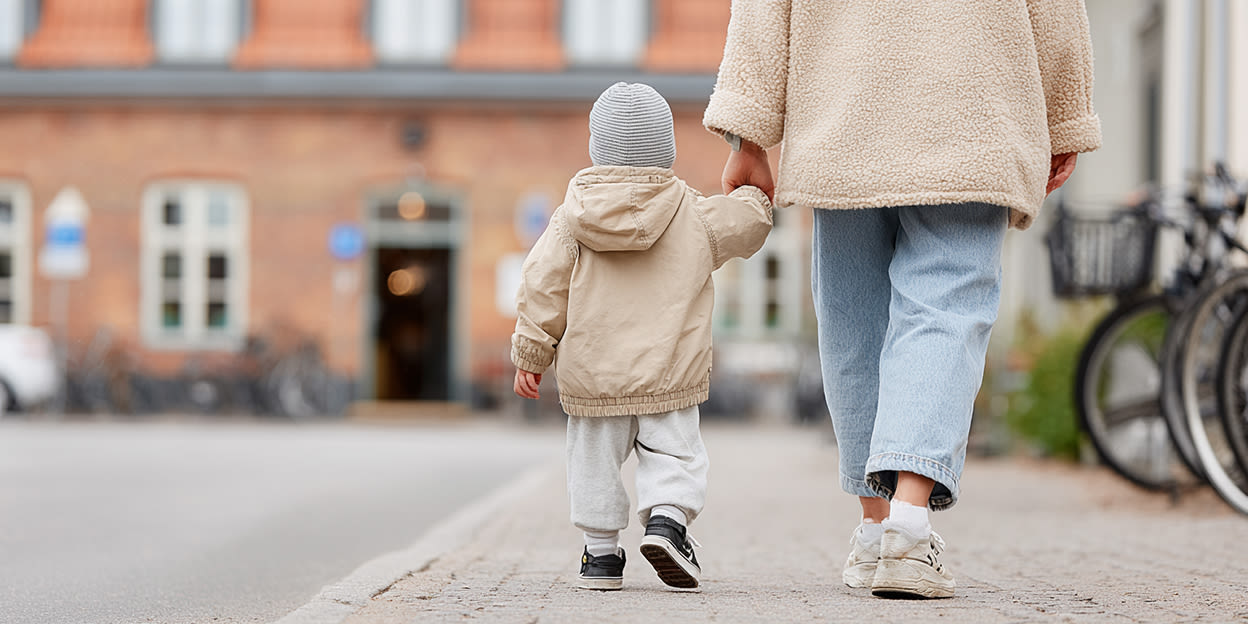 Litet barn går på trottoaren och håller sin förälder i handen.