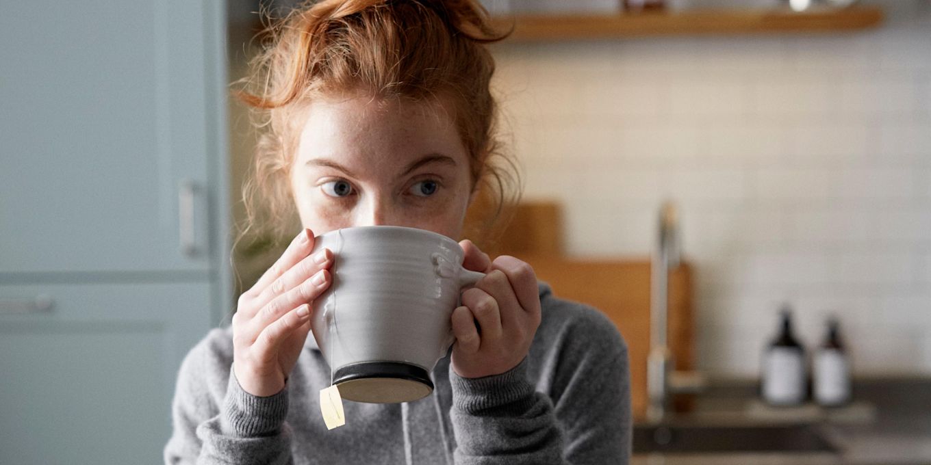 Tjej står i köket och dricker ur en temugg.