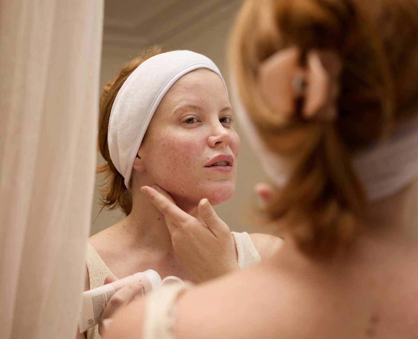 Tjej tittar sig i spegeln och drar några fingrar under kindbenet. Hon har ett hårband som håller undan håret.