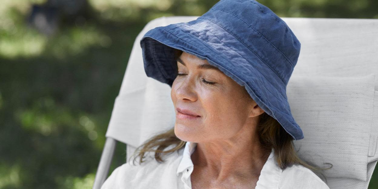 Person sitter utomhus med en solhatt som skyddar ansikte och huvud från solen. Bilden illustrerar egenvård och hur man kan hantera förändringar i hud och utseende under en cancerbehandling.