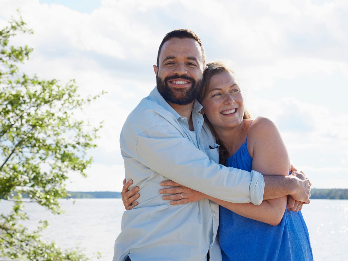 Man och kvinna står utomhus i solskenet och kramar om varandra.