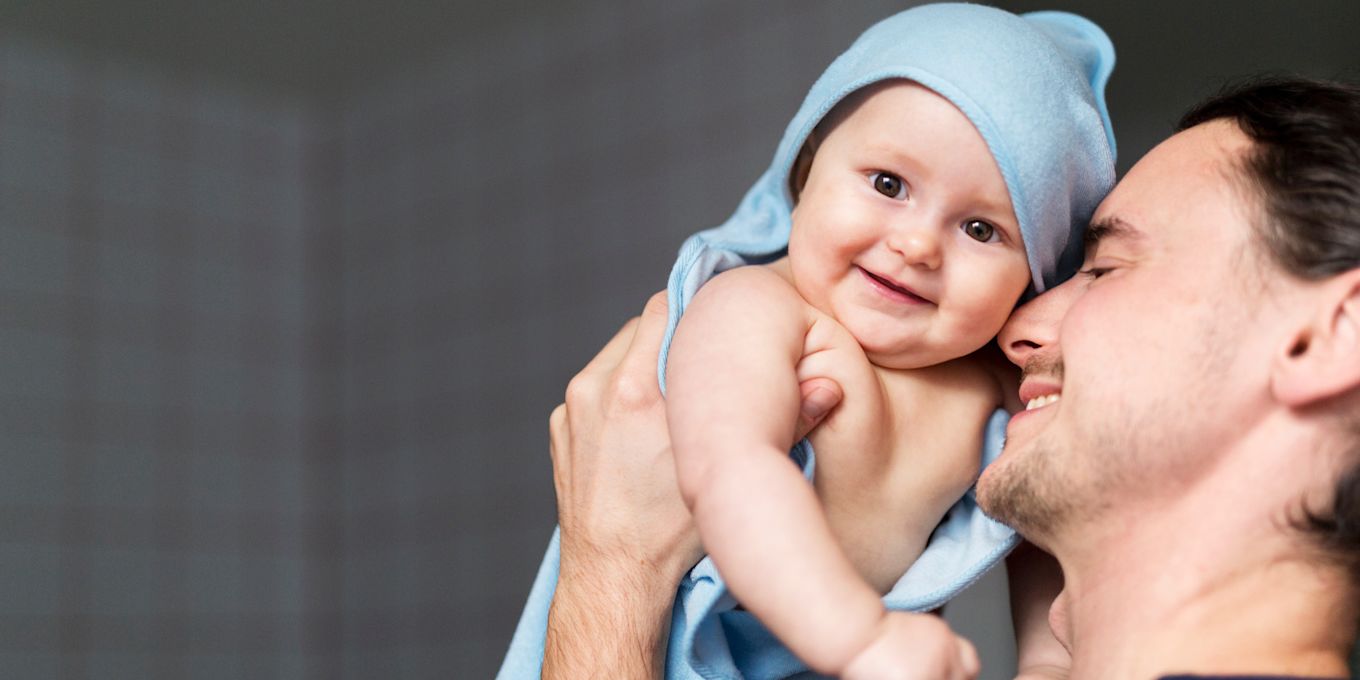 Pappa ler och håller upp nybadad bebis, insvept i handduk. 