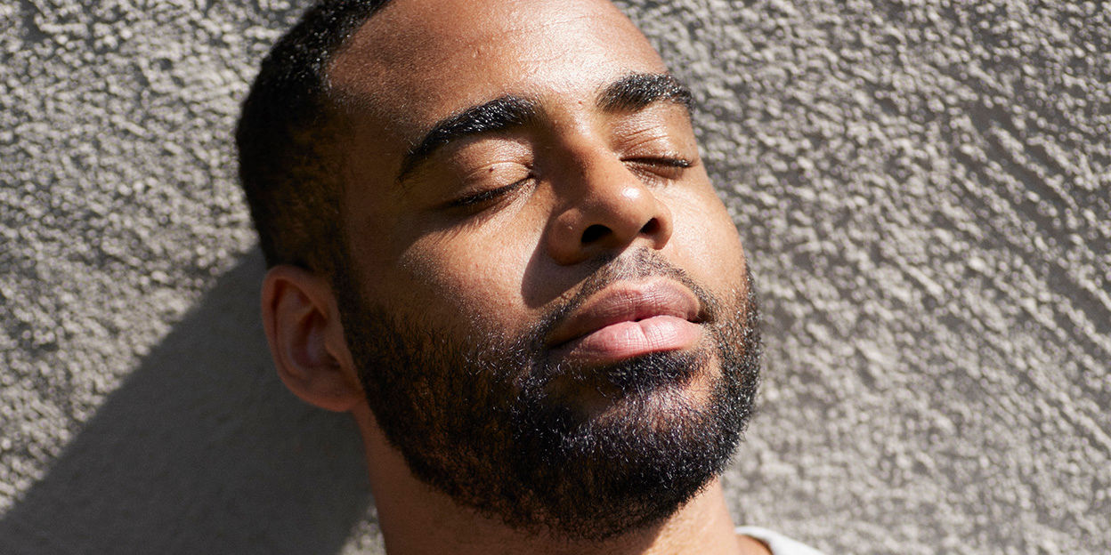 En man står mot en vägg och blundar i solen. 