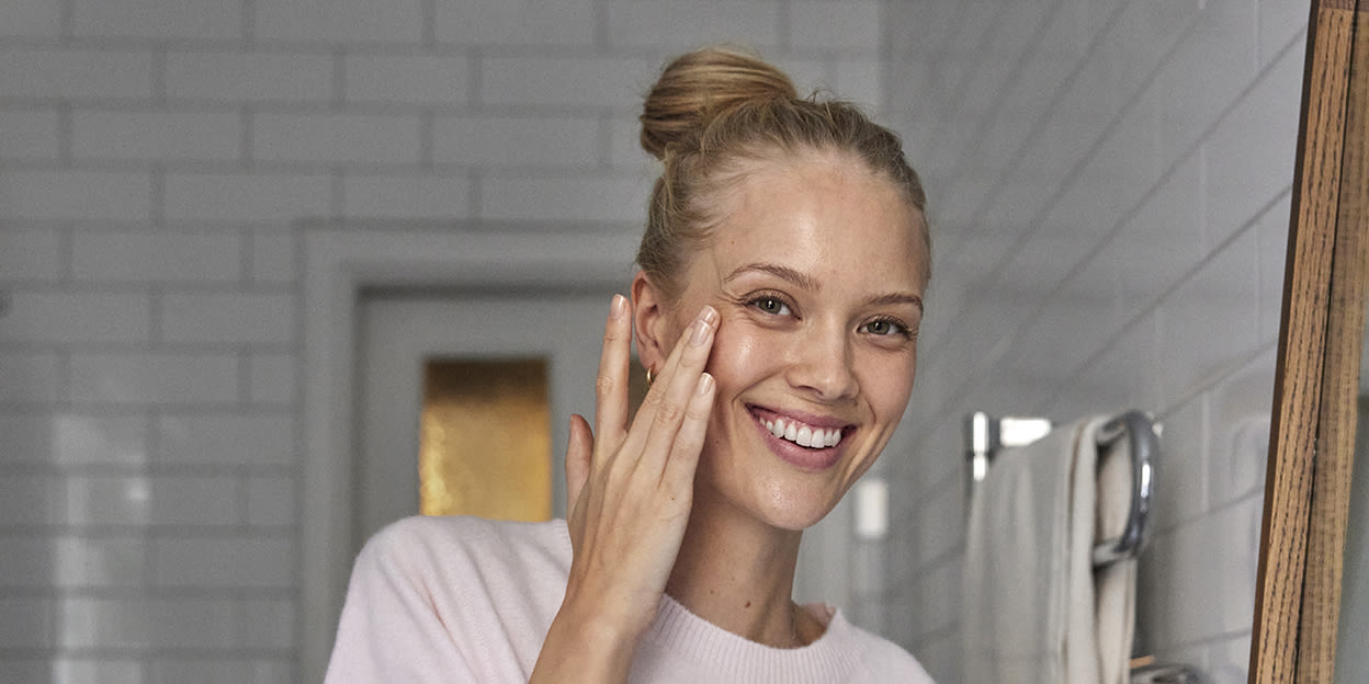 Kvinna ler glatt samtidigt som hon applicerar ögonkräm