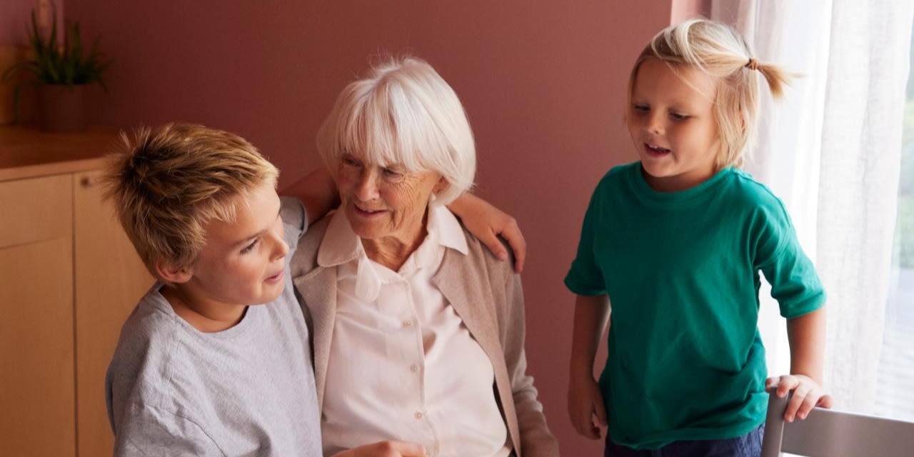 Två barn sitter med sin mormor eller farmor vid ett bord.