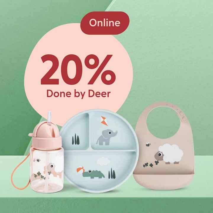Barnmatsset med rosa nappflaska, blå delad tallrik med elefant och krokodilillustration och beige haklapp med fårmotiv framför en grön bakgrund och en rosa cirkel med texten "20% Done by Deer Online".