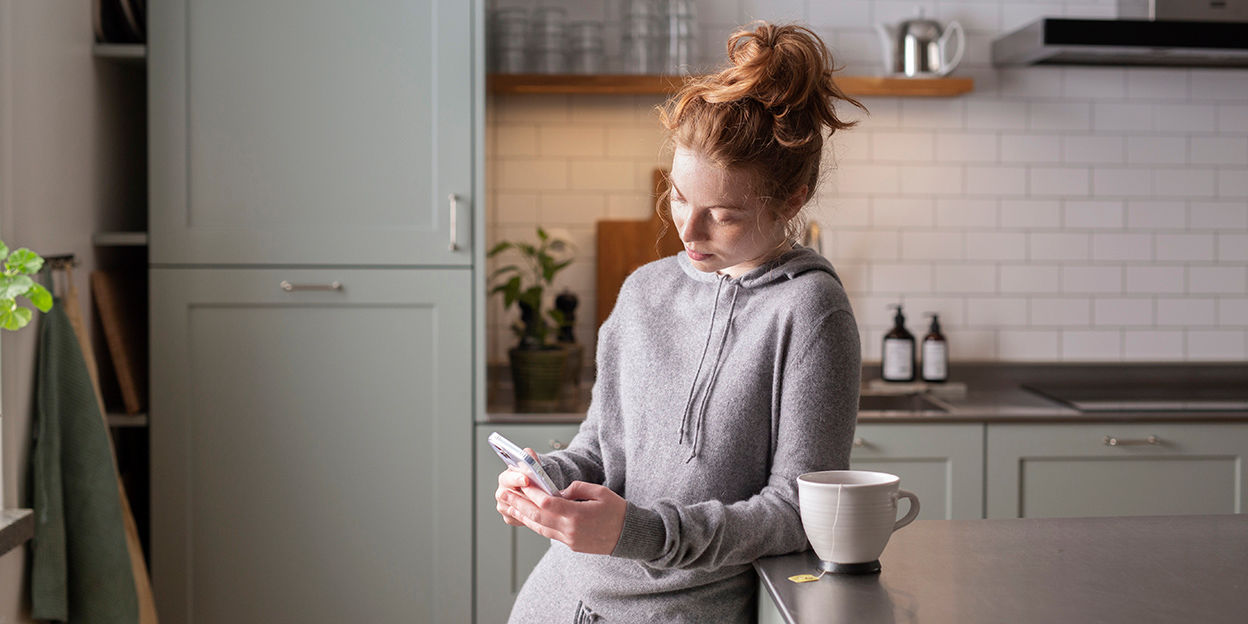 Kvinna står vid en köksö och har en stor kopp te bredvid sig. 