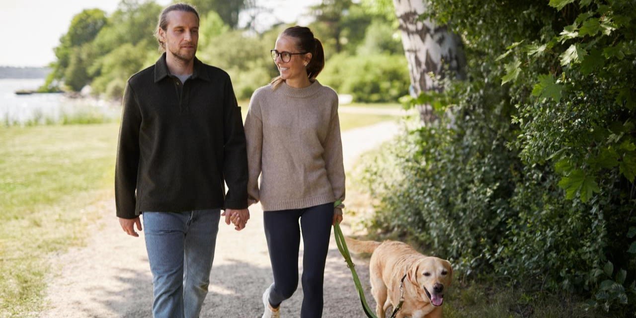 Man och kvinna är ute och går med en hund på en promenadstig.