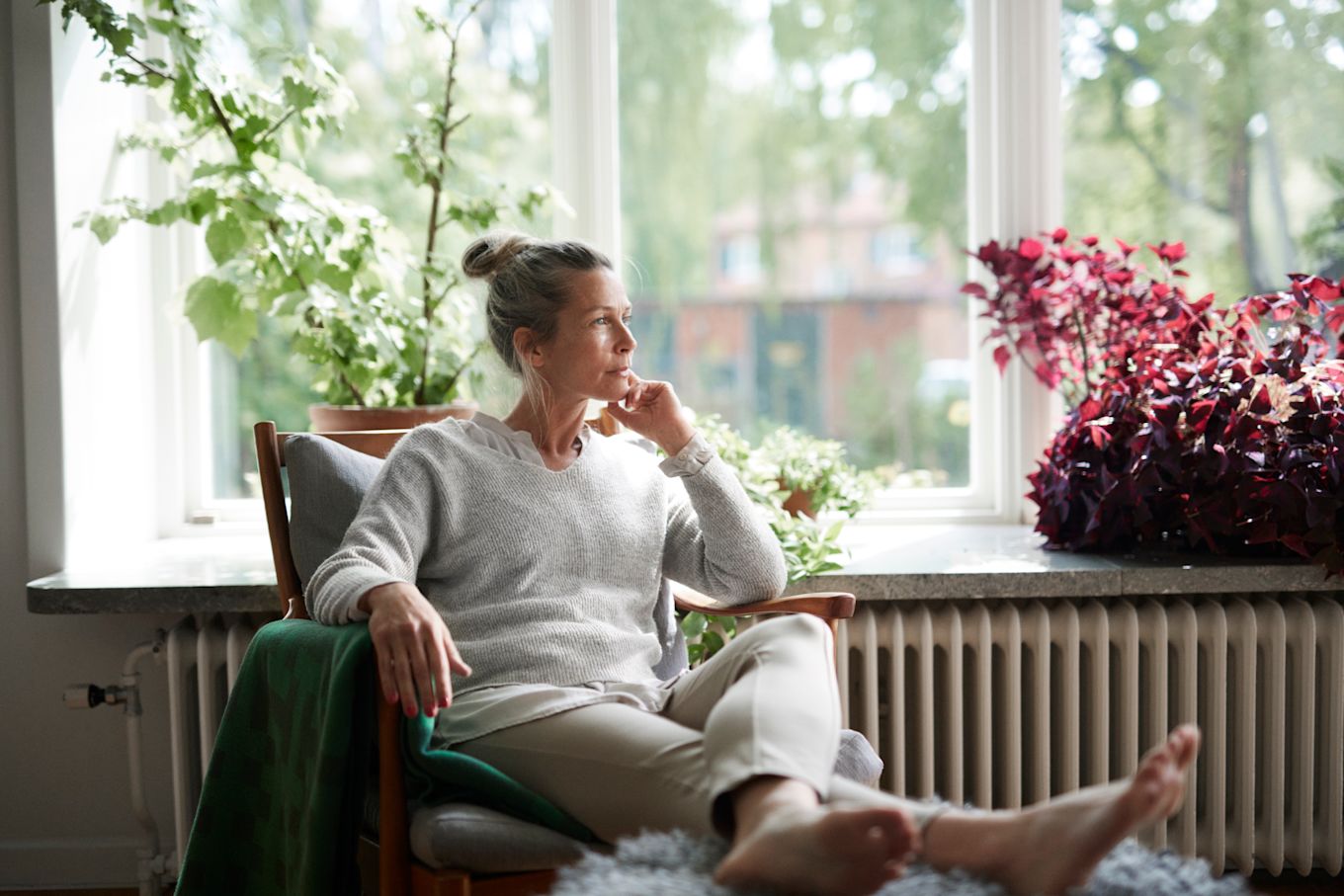 Kvinna sitter i fåtölj i vardagsrum och tittar åt sidan.