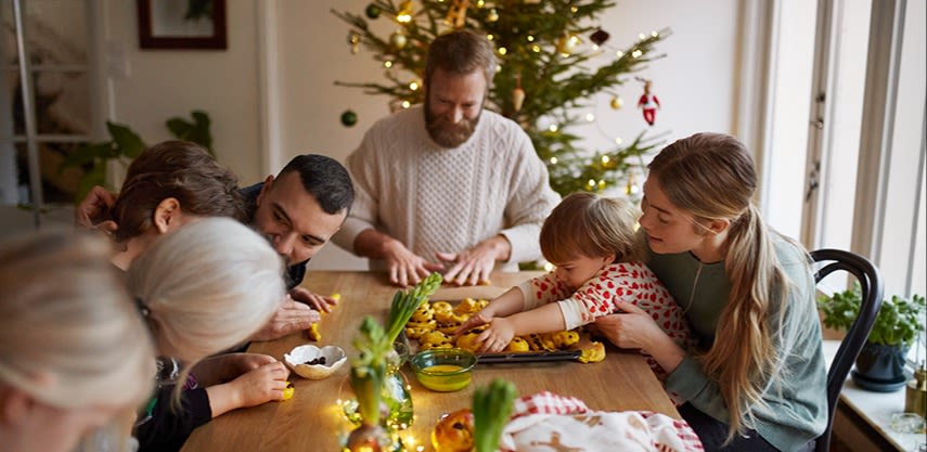 En familj som bakar lussekatter i ett julpyntat kök.