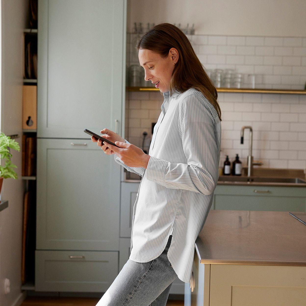 Kvinna står i köket och tittar ner på sin mobiltelefon.