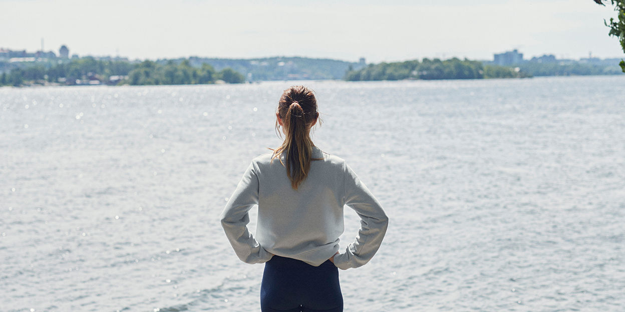 Kvinna står med ryggen mot kameran och kollar ut mot havet. 