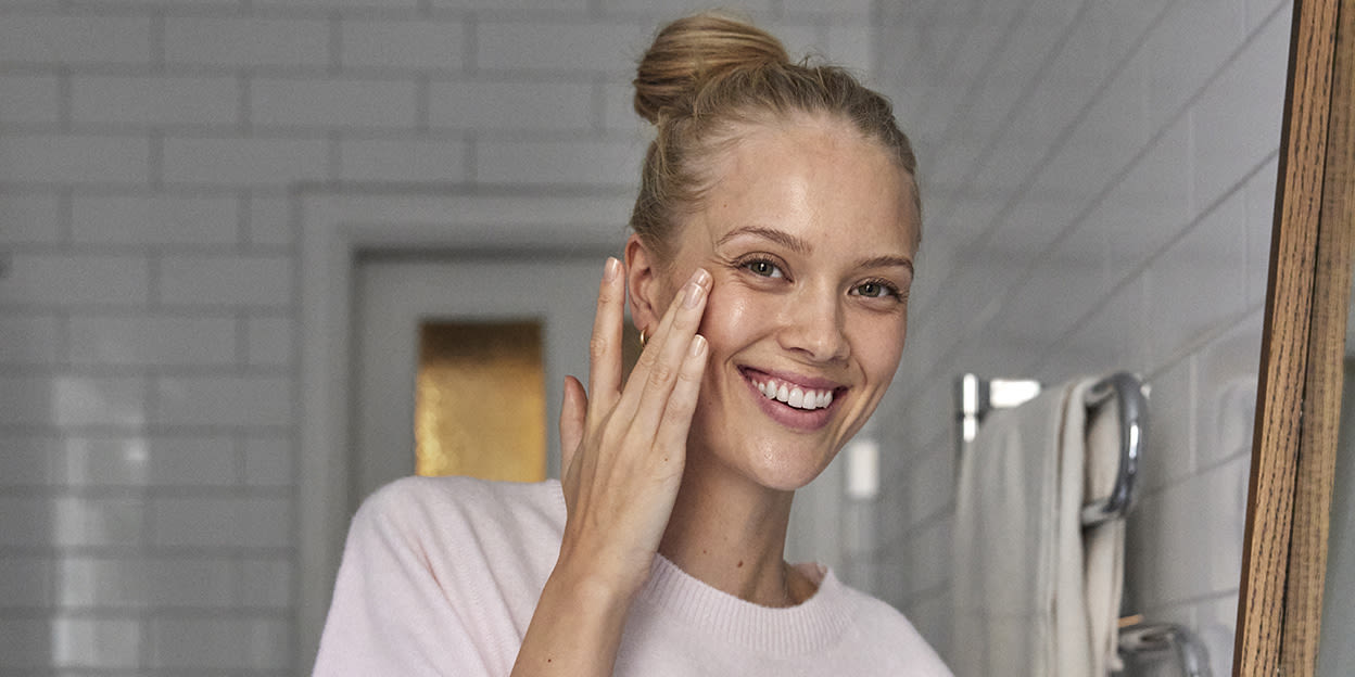 Ung kvinna står i badrummet och utför hudvårdsrutin.