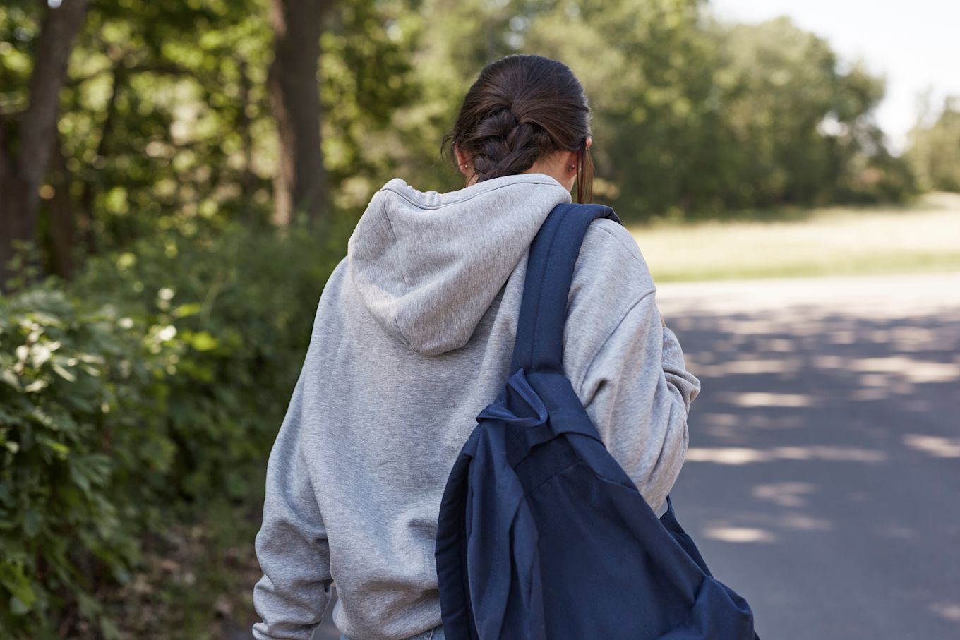 Tonårstjej som går iväg med nedböjt huvud, iklädd munktröja med en ryggsäck över ena axeln.