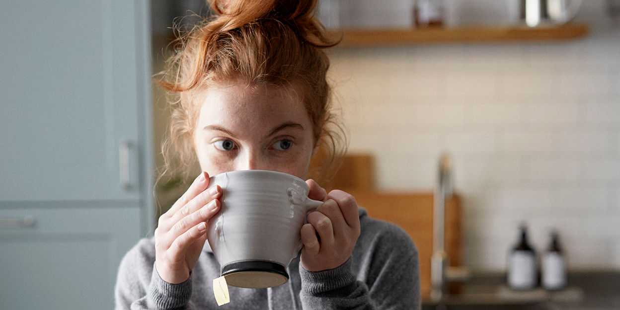 Tjej står i köket och dricker ur en temugg.