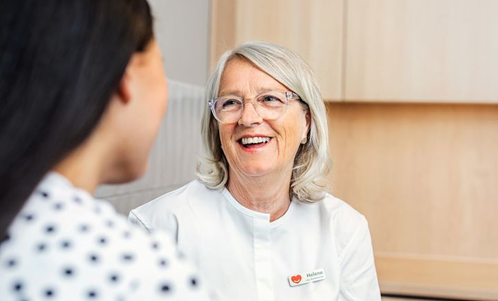 Sköterska i vit klädsel ler mot en patient.