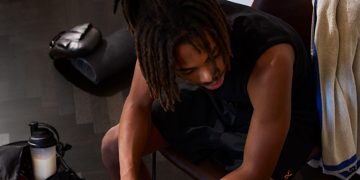 Ung  kille sitter på en stol inne på gymmet omgiven av sina träningstillbehör.