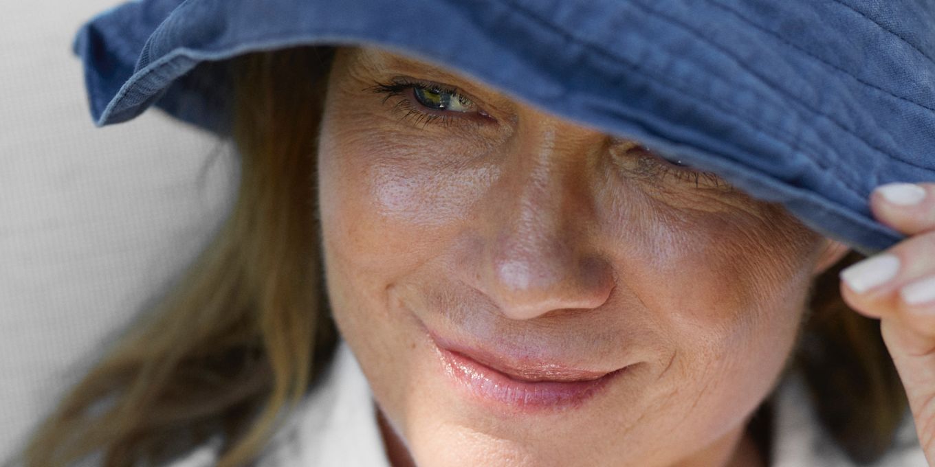 Kvinna sitter utomhus i skuggan med en solhatt på huvudet och tittar åt sidan.