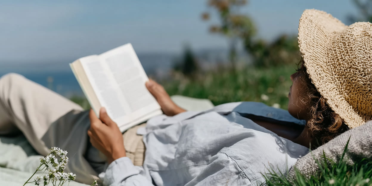 Kvinna ligger i gräset och läser en bok i solen. Bilden är delvis skapas med AI.