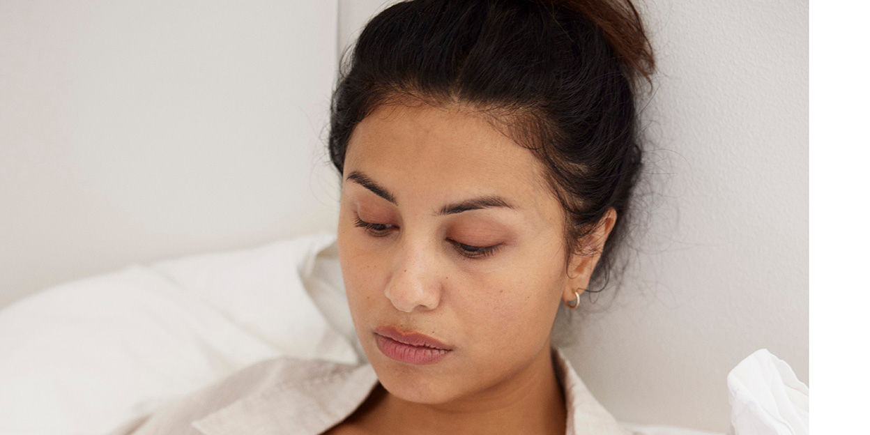 Tjej sitter i sängen med sänkt blick och ser hängig ut.