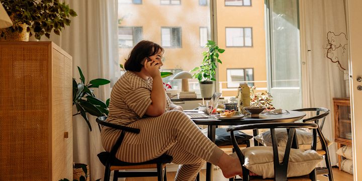 Tjej i randig pyjamas sitter vid köksbordet och pratar i sin telefon.