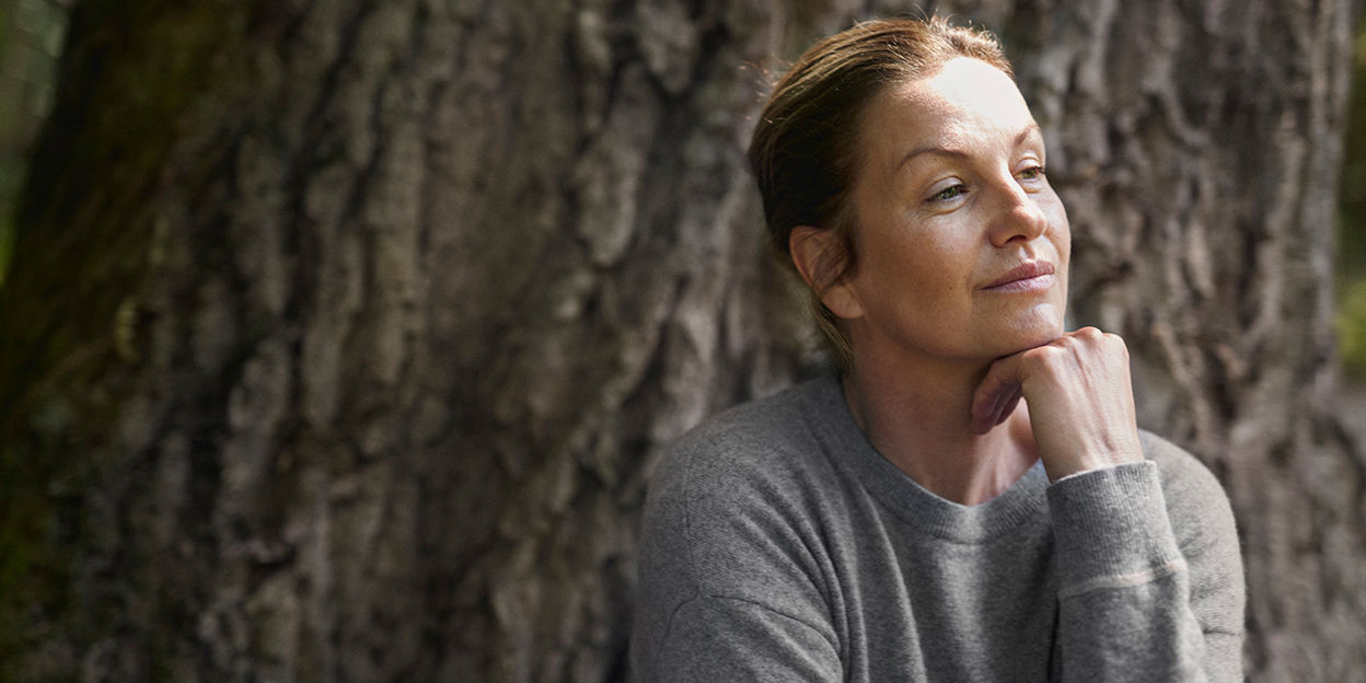 En kvinna sitter utomhus vid en träd och tänker. 
