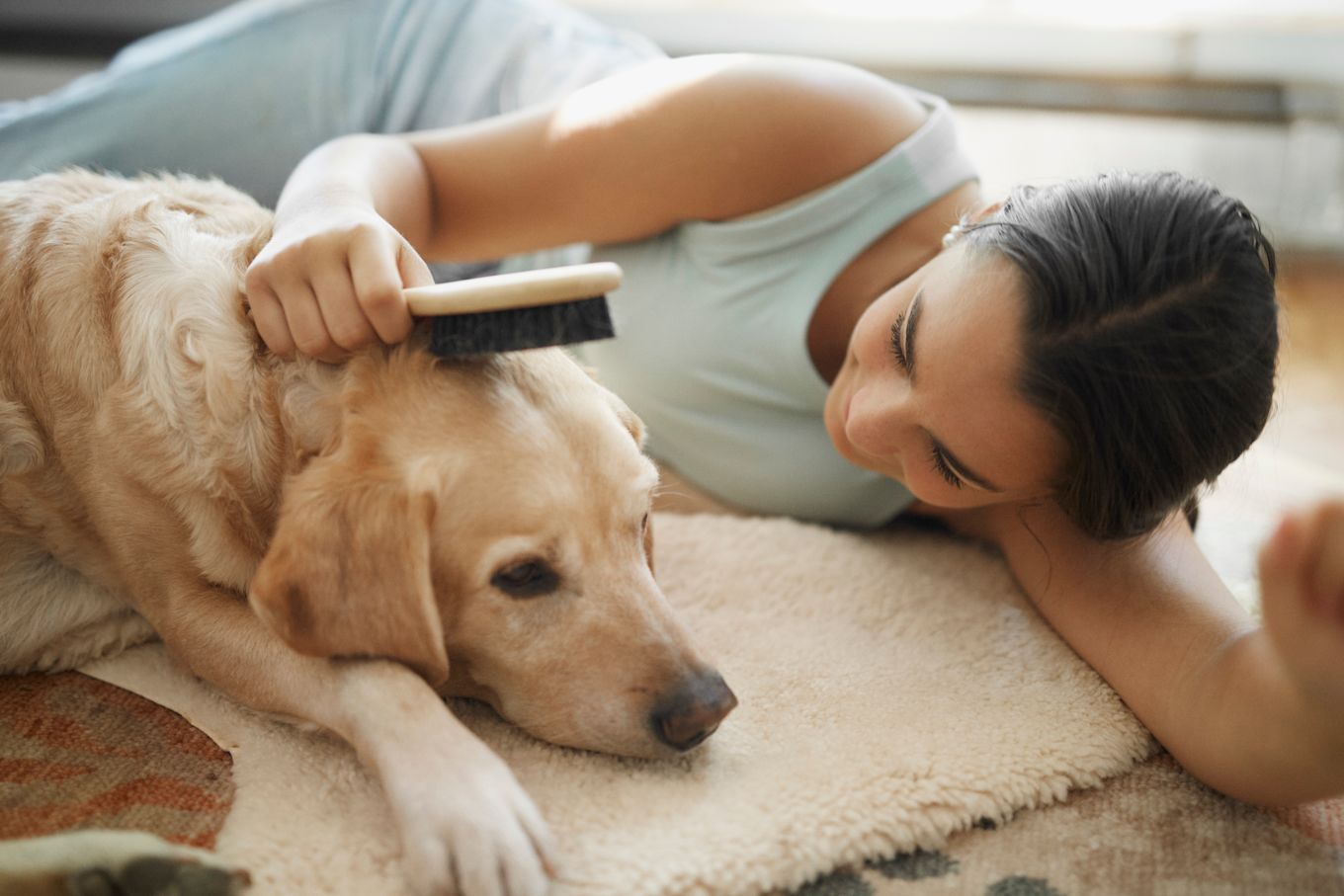 Tjej ligger på golvet tillsammans med en hund som hon borstar på huvudet.