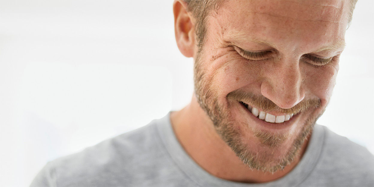 Man i badrum som ser glad ut och tittar ner mot golvet. Stort leende. 